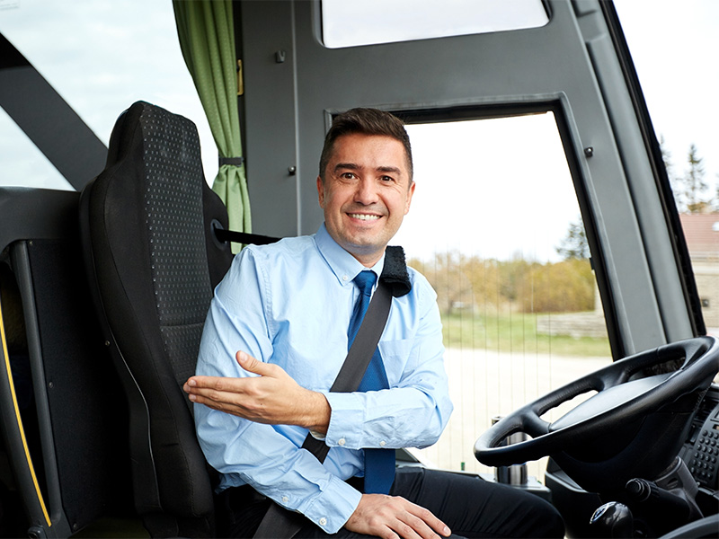 Freundlicher Busfahrer begrüßt Fahrgäste am Einstieg eines modernen Reisebusses und lädt zum Einsteigen ein.