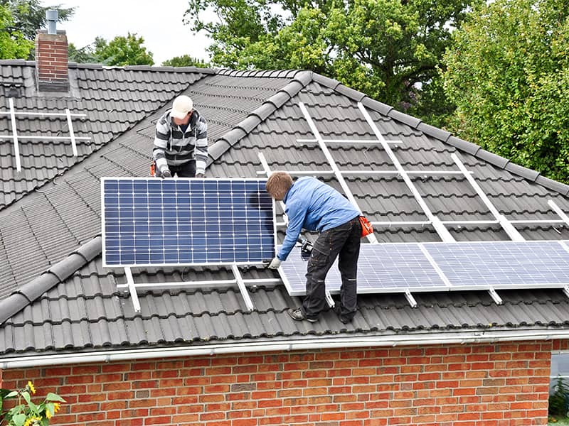 Zwei Dachdecker montieren Solarzellen auf einem Wohnhausdach in Hamm