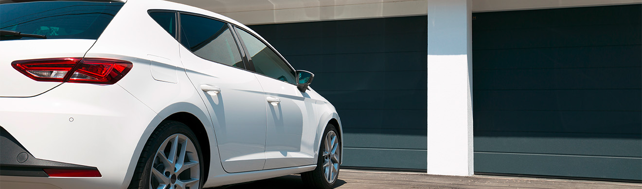 Weißes Auto wartet vor modernem Haus mit großem Garagentor – hochwertige Garagentore in Hamm zeigen Komfort.