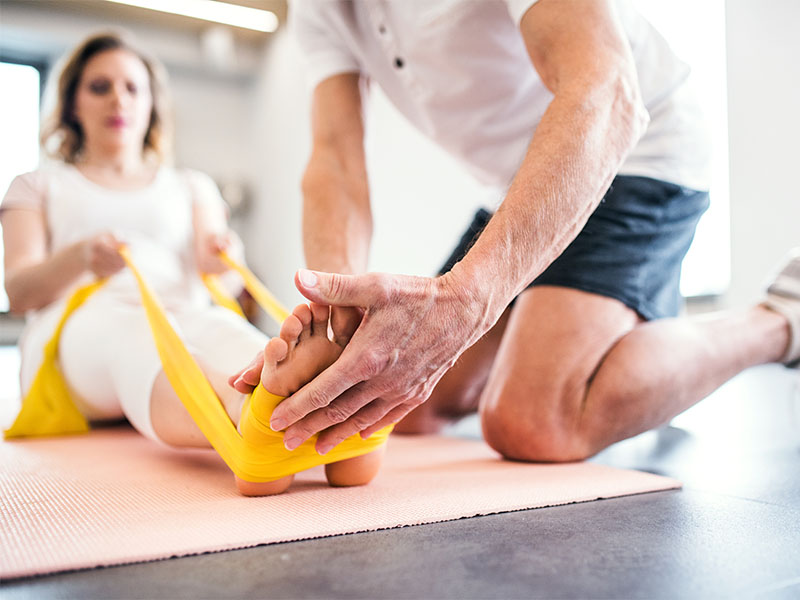 Bei der Physiotherapie in Bergkamen führt ein Physiotherapeut mit einer weiblichen Patientin mit dem Theraband Übungen für den Rücken durch